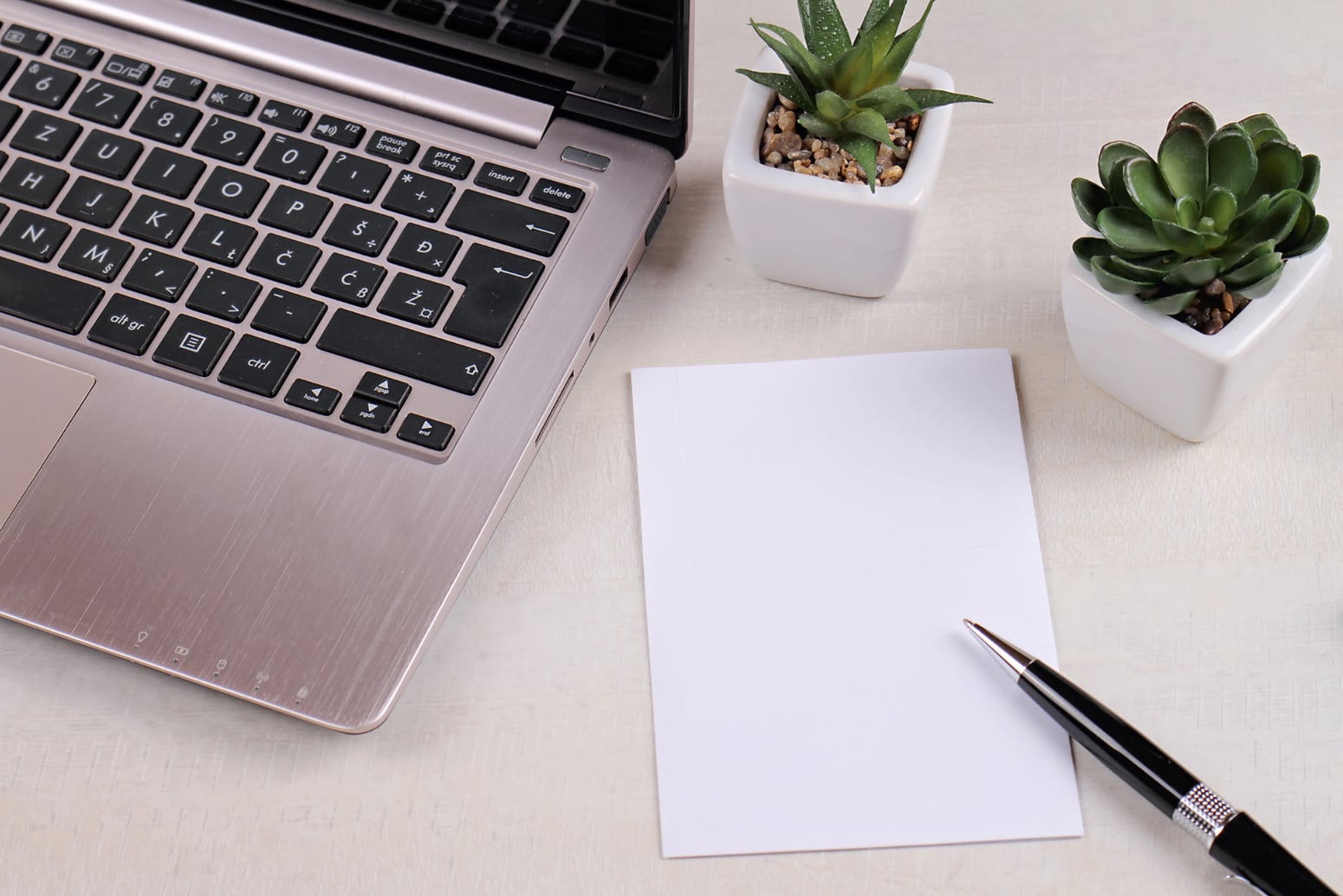 Laptop computer, succulents, blank paper on office desk.